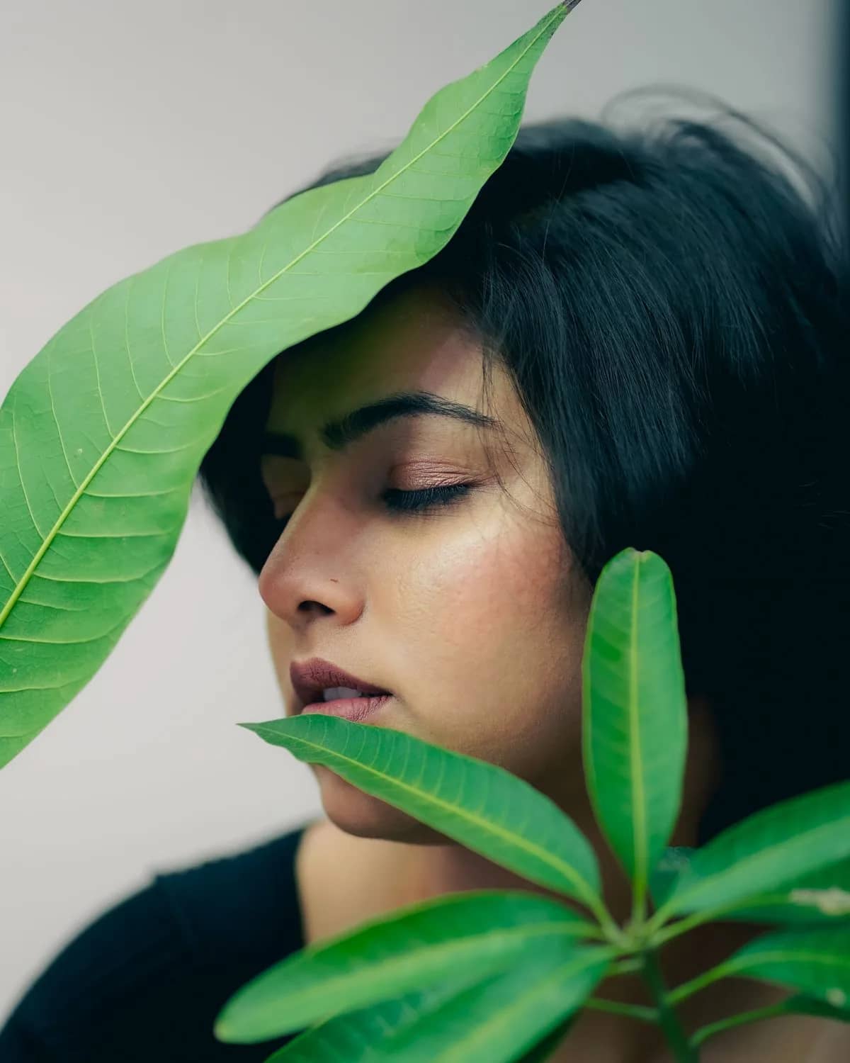 Woman with eyes closed framed by green leaves