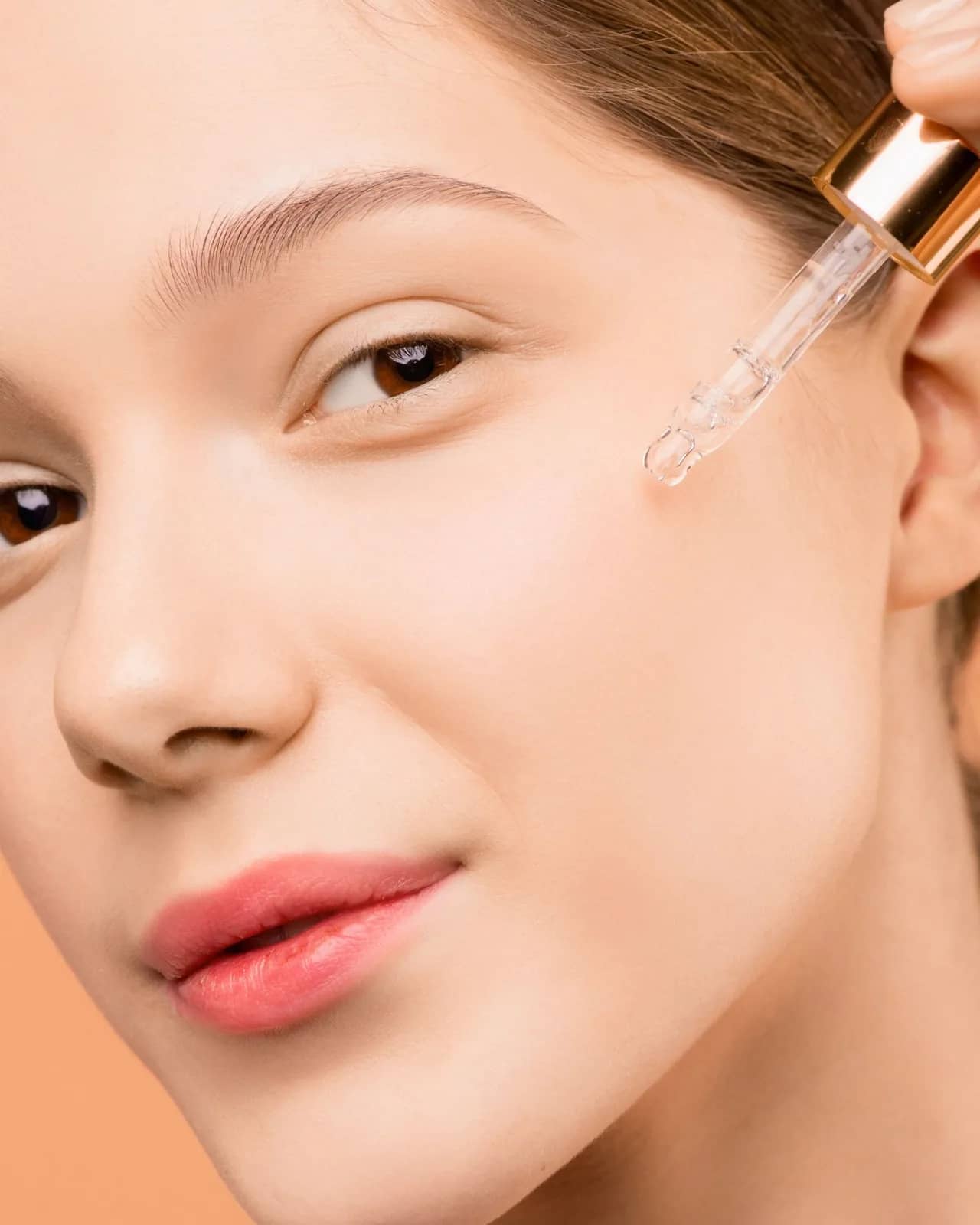 Woman applying a drop of face serum to her cheek